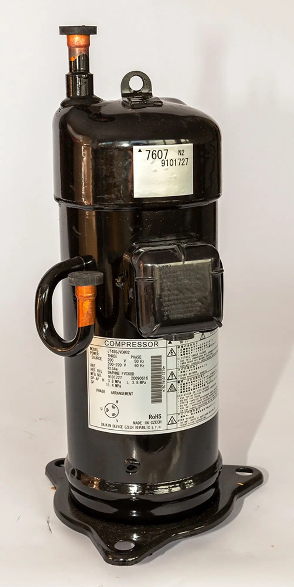 Schwarzer Daikin Kompressor mit zwei Anschlüssen und einem montierten Sockel. Auf der Vorderseite befinden sich technische Daten und Warnhinweise.